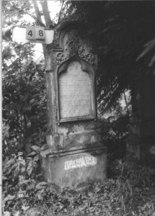Grabstein 48 (Index: 99799505) Material: Sandstein, Schriftplatte Marmor Zustand: leicht verwittert Maße HxBxT: 154x49x20 cm Beschreibung: Stele, eingezogener Stelzbogenabschluß, eingelassene Schriftplatte mit Kleeblattbogenabschluß, getreppter Sockel Symbolik: Voluten, Ranken: Grabstein 48