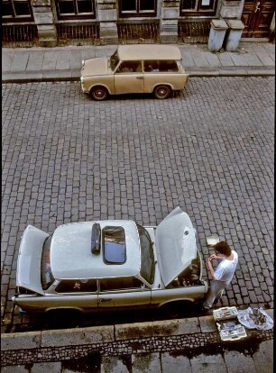 Leipzig, März 1992. Trabant und Trabant Kombi am Straßenrand auf Kopfsteinpflaster. Ein PKW wird repariert