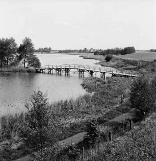 Herrenteich: Fischhuser Damm: hölzerne Fußgängerbrücke: Blick Richtung Nordosten auf oberen Herrenteich: im Vordergrund Ufer mit Schilf, Büsche, Zaun, Wanderweg
