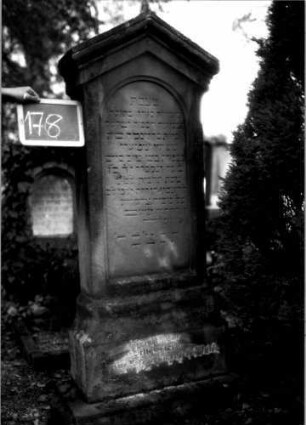 Grabstein 178 (Index: 100109711) Material: Sandstein Zustand: verwittert Maße HxBxT: 170x63x24 cm Beschreibung: Stele, getreppter Sockel, giebelartiger Abschluß mit Verdachung, Schriftfeld eingetieft mit Rundbogenabschluß: Grabstein 178