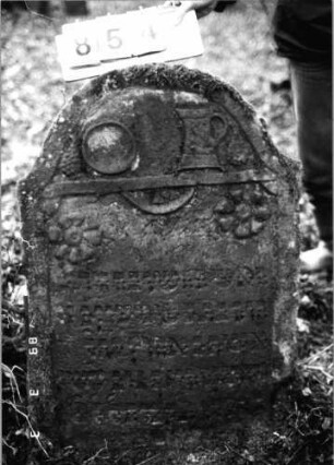 Grabstein 854 (Index: 99751248) Material: Sandstein Zustand: verwittert Maße HxBxT: 102x69x15 cm Beschreibung: Stele, eingezogener Rundbogenabschluß, rechteckiges Schriftfeld eingetieft Symbolik: Kanne mit Schale, zwei Blüten, Trauben: Grabstein 854