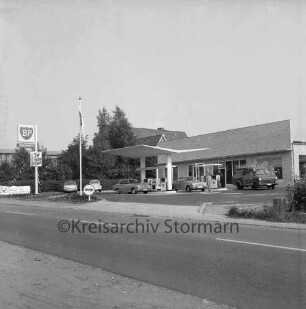 BP-Tankstelle: Hamburger Straße: Neubau: rechts Gebäude: davor Zapfsäulen mit tankenden Pkws, Kleintransporter und Personen: links BP-Schild und parkende Pkws: dahinter Bäume und Wohnhäuser