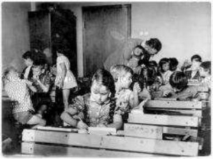 Mädchen und Jungen in Schulbänken, im Hintergrund ein Lehrer