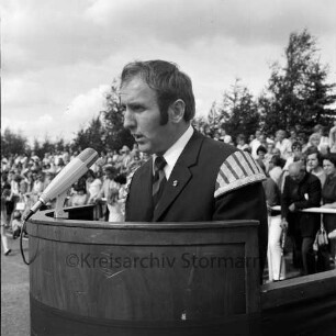 "Old Reinfelder Jungs e.V.": 25-jähriges Jubiläum: Musikfest: Stadion am Bischofsteicher Weg: Vorsitzender Claus Sellmer bei Begrüßungsrede: Rednerpult mit Mikrofon: im Hintergrund Zuschauer, 18. August 1974