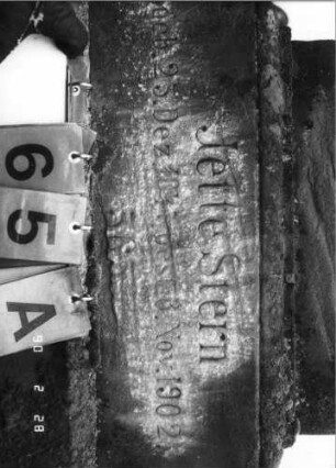 Grabstein 65 (Index: 100114879) Material: Sandstein Zustand: beschädigt am Giebel, sehr stark verwittert am Sockel, sonst leicht verwittert, Textplatte fehlt Maße HxBxT: 238x65x31 cm Beschreibung: Stele auf gestuftem Sockel, eingezogener Rundbogen mit Akroter und Voluten, Blatt im Giebel, eingesetzte Textplatte: Grabstein 65A