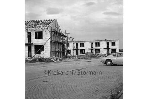 Kolberg-Körlin-Straße: Mehrfamilienhaus im Rohbau mit Gerüst und Dachsparren: davor Baumaterial: hinten rechts weiteres Haus im Bau: vorn rechts Parkplatz mit Pkw