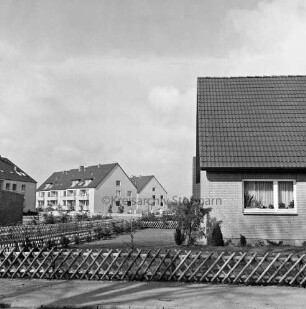 Neubausiedlung "Im Weeden": rechts Einfamilienhaus mit Vorgarten und Jägerzaun: hinten links Wohnblocks: dazwischen Fußweg