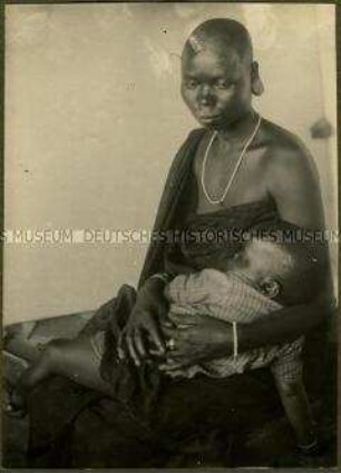 Sitzende Massai-Frau mit schlafendem Kleinkind von links