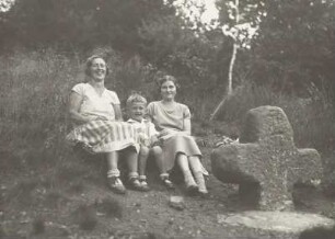 Steinkreuz mit eingeritztem Dolch (Sühnekreuz) : Pirna-Graupa. Borsbergwald, Kreuzergrundweg. Die Frau des Fotografen mit älterem Sohn und Freundin aus Bremen, an einem Steinkreuz (Sandstein; 135 x 90 x 32 cm) sitzend