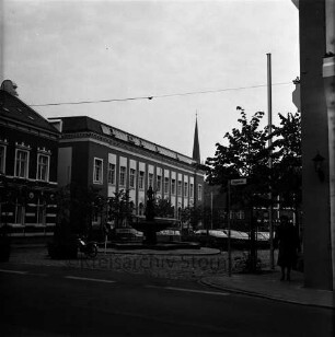 Markt: vorne die Hagenstraße, mittig der Gänselieselbrunnen, dahinter parkende Fahrzeuge, links das Stadthaus, vorne rechts Passantin auf dem Gehweg, im Hintergrund Gebäude der Hindenburgstraße, Blick Richtung Süden