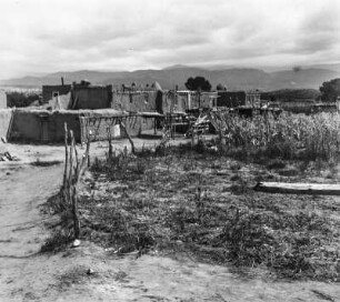 Tesuque-Pueblo : Blick auf ein Pueblo der Tesuque im Bundesstaat New Mexico. Am linken Bildrand Adobe-Häuser mit Verputz aus hellem Lehm, rechts ein Maisfeld.