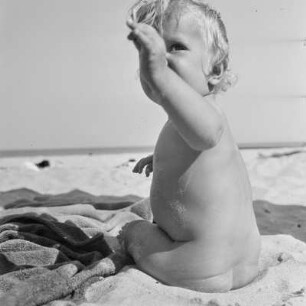 Kleinkind sitzt auf einer Decke am Strand