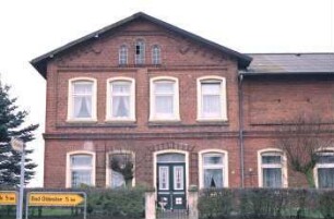 Hauptstraße 26: Bauernhaus aus Backstein, mit umlaufendem Gesims: giebelständiges Wohnhaus: Straßenfront mit Eingangstür: rechts traufständiger Wirtschaftstrakt [angeschnitten]: vorne Gartenhecke, Eingangspforte: vorne links Hinweisschilder nach Bad Oldesloe, Schulenburg