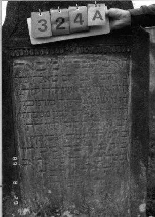 Grabstein 324 (Index: 100107748) Material: heller Sandstein Zustand: stark verwittert, teilweiser Textverlust Maße HxBxT: 176x41x14 cm Beschreibung: Stele, Abschluß Sonderform (geschwungen eingezogener flacher Kleeblattbogen), Schriftfeld rechteckig eingetieft Symbolik: Blüte, Halbblüte, Tropfenband: Grabstein 324A