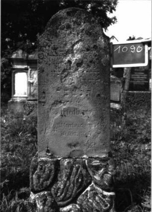 Grabstein 1090 (Index: 100104143) Material: Sandstein Zustand: stark verwittert, Zerstörungs- und Reparaturspuren Maße HxBxT: 164x51x17 cm Beschreibung: aufgesockelte Stele mit Konvexbogenabschluss, Sockel felsenartig gearbeitet: Grabstein 1090