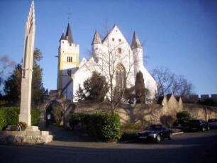 Ansicht von Westen mit Kirche (Kirchturm romanisch gegründet-Langhaus Gotisch neu erbaut mit rundem Treppentürmen in der Giebelseite) über innerer Kirchhofmauer (Wehrgang abgetragen)