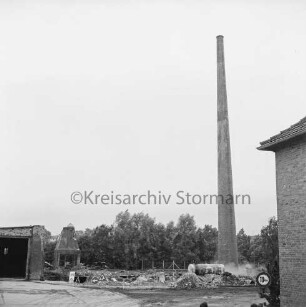 Stadtwerke Bad Oldesloe: Gaswerk: Lübecker Straße: Sprengung des Schornsteins des abgerissenen Kraftwerks: rechts Gebäudeecke: dahinter leicht geneigter Schornstein mit Gastank, am Fuß Rauchwolken: hinten Bauschutt: links teilweise abgerissenes Gebäude: hinten Bäume: 10. Juni 1971