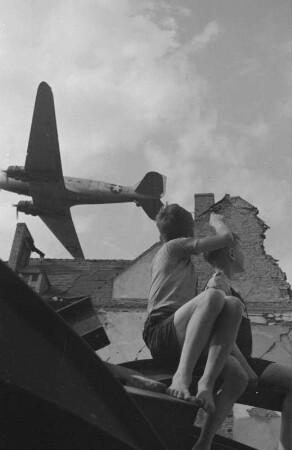 Berlin (West). "Zaungast der Luftbrücke". Zwei Jungen beobachten aus einer Hausruine ein tieffliegendes Transportflugzeug ("Rosinenbomber")