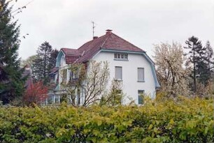 An den Stücken 5: traufständiges Wohnhaus: Straßenfront, in Erdgeschoss verglaste Veranda, an Mansarddach Zwerchgiebel, darin Loggia: Giebelseite: im Vordergrund Hecke