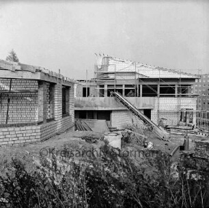 Evangelisches Gemeindehaus: Masurenweg: Rohbau: davor Erdhaufen, Bretterhaufen, Baumaterial, Förderband und Gestrüpp: hinten rechts Hochhäuser