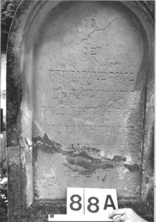 Grabstein 88 (Index: 100114221) Material: Sandstein Zustand: stark verwittert mit großem Textverlust, gebrochen und repariert Maße HxBxT: 187x59x28 cm Beschreibung: Stele, Sockel, Rundbogenabschluß mit Mittelakroter, deutsches eingetieftes Schriftfeld rechteckig Symbolik: Palmette als Mittelakroter: Grabstein 88A
