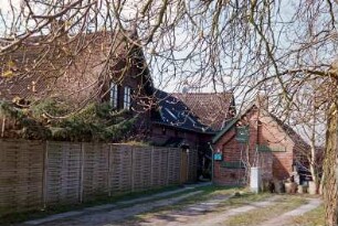 Blumendorf 8: traufständiges Mehrfamilienhaus aus Backstein: Rückfront: umlaufendes Gesims, Hintertür mit Verdachung, an beiden Seiten Querbauten mit Giebelzier: davor Sichtschutzzaun, rechts Nebengebäude aus Backstein
