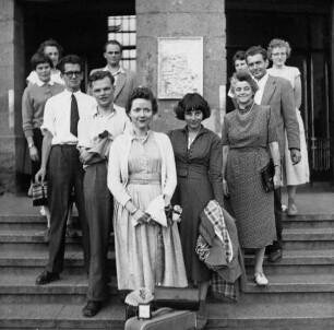 Studierende und Mitglieder des Kunstgeschichtlichen Seminars Marburg, darunter Maria Wenzel (hinten links), Rudolf Fischbach (links neben dem Pfeiler), Herwarth Röttgen (mit Schlips), Hans-Joachim Kunst (vorne), Brigitte Sauerländer (vorne, mit Mantel über dem Arm), Frieda Dettweiler (mit Handtasche) und Herbert Köllner (hinten rechts), auf den Stufen des Marburger Bahnhofs