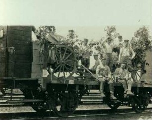 Blumengeschmückte Soldaten auf Eisenbahnwagen auf der Fahrt an die Front
