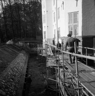 Restaurierung: innerer Graben: neue Grabenversteifung mit Holzbohlen am Grabenfuß: Grabenböschung nach Wiederherstellung mit alten Findlingen: Arbeiter auf Gerüst an Fundament