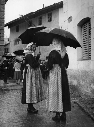 Sarnthein (Bozen). Frauen in Trachten und mit Regenschirmen