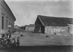 Straßenansicht : Blick auf eine Straße in einer Siedlung. Am linken Bildrand ein landwirtschaftliches Gerät.