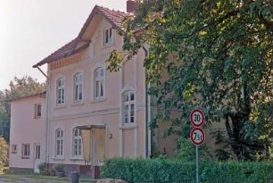Bahnhofstraße 53: ehemaliges Bahnhofsgebäude der Südstormarnschen Kreisbahn: Traufseite an Ladestraße mit Eingangstür, Frontispiz, links Anbau: Hecke, Baum, Verkehrsschilder