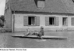Zwei Jungen im Paddelboot vor einem Haus