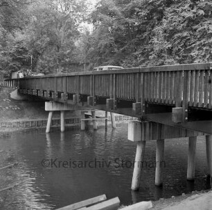 Travebrücke: Landstraße zwischen Nütschau und Schlamersdorf: Nütschauer Weg: Brückenbau: Holzbrücke auf Betonpfeilern vor Fertigstellung: darauf Baufahrzeug und Bagger: vorn Trave: am Ufer Holzbohlen