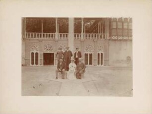 Gruppenportrait : Portraitaufnahme von einer Frau mit Kind und fünf Männern in einem Innenhof in Bagdad. Rechts vorne der Geograph Hugo Grothe (1869-1954).