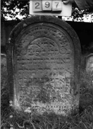 Grabstein 297 (Index: 100107700) Material: heller Sandstein Zustand: stark verwittert und versalzen, weitgehender Textverlust Maße HxBxT: 91x62x13 cm Beschreibung: Stele mit Rundbogenabschluß, Schriftfeld eingetieft: Grabstein 297
