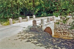 Schäperbarg: Granitquaderbrücke über die Barnitz: Sanierung: Fertigstellung: Seitenansicht: Stirnwand, Flügelwand, oben Granitpoller mit Geländer, Fahrbahn, Arbeiter: im Vordergrund Neuanlage der Böschung