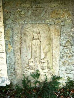 Friedhof im Norden-Mauerrest ist beschädigtem Grabstein-Umschrift und Personendarstellung in halbplastischer Weise