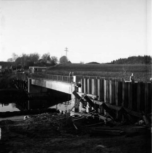 Trave: Brückenbau: Hauptstraße: Landstraße zwischen Klein Wesenberg und Groß Wesenberg: Verbreiterung der einspurigen Brücke: vorn rechts Spundwände: daneben und oben Arbeiter: hinten links Bauwagen, Lieferwagen und Pkws: dahinter Häuser und Bäume