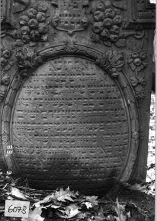 Grabstein 607 (Index: 99753121) Material: Sandstein Zustand: gut, Stele eingesunken Maße HxBxT: 138x78x13 cm Beschreibung: Stele, eingezog. Kielbogenabschluß, ovales Schriftfeld Symbolik: Wappenschild, Feigen, Trauben, Lorberkranz, Blätter, Schriftband: Grabstein 607B