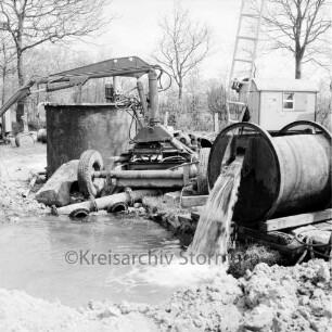 Wasserversorgung: Mühlenwiese: Tiefbrunnen: Pumpanlage mit Rohren: vorn Erde und Wasserlache: hinten Mitte Bagger: dahinter rechts Baubude: links Tonnen: hinten Bäume