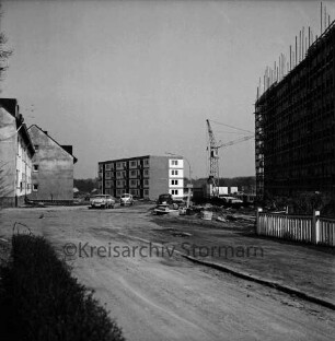 Schanzenbarg: vorn rechts hinter Zaun eingerüsteter Wohnblock im Bau: links zweigeschossige Wohngebäude: hinten Mitte Wohnblock vor Fertigstellung, Baukran, Fundament und Grundmauern eines weiteren Wohnblocks: davor parkende Pkws, VW-Bus, Baumaterial: vorn unbefestigte Straße