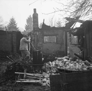 Brand: Sieker Landstraße: Behelfsheim: Brandruine: Innenraum: darin Mauerwerk und verbrannte Gegenstände: hinten rechts im Eingang Polizist: links Brandsachverständiger beim Fotografieren: hinten Bäume