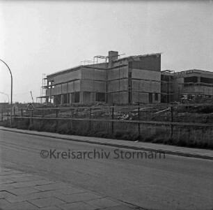 Evangelisches Gemeindehaus: Masurenweg: Rohbau: vorn Straße, Bauzaun, Erdhaufen, Baumaterial: links Verkehrsschild und Straßenlampe