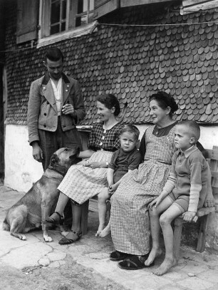 Familie mit Schäferhund, auf einer Bank vor dem Haus sitzend