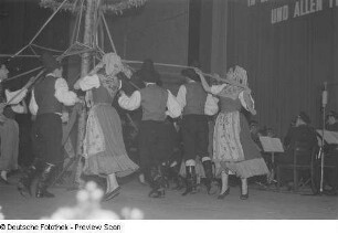 Menschen in Tracht tanzen bei einer Veranstaltung zum Gedenken an die Völkerschlacht mit Bändern in der Hand um einen Maibaum, im Hintergrund ein Orchester