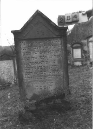 Grabstein 284 (Index: 99609008) Material: Sandstein Zustand: stärker verwittert Maße HxBxT: 133x61x13 cm Beschreibung: Stele auf Sockel, eingezogener Giebel mit Mäanderfries, Schriftfeld eingetieft: Grabstein 284