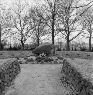 Ehrenmal: Anlage mit Findling und Feldsteinen: davor Blumen: im Hintergrund Baumreihe