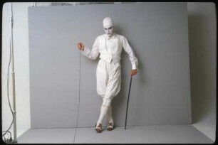 Fotoshooting einer Performance- oder Schauspielgruppe : Ingolf Thiel in weißem Kostüm, Mit Spazierstock und weiß geschminktem Gesicht vor einem grauen Hintergrund