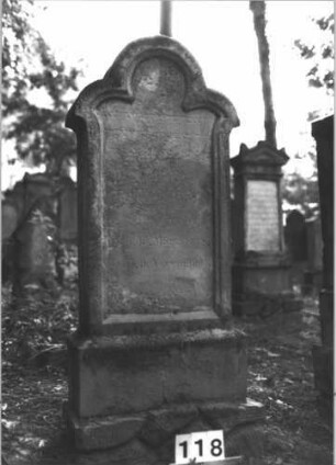 Grabstein 118 (Index: 99898916) Material: Sandstein Zustand: stark verwittert Maße HxBxT: 137x57x20 cm Beschreibung: aufgesockelte Stele mit seitlich spitz auskragendem Dreipassbogenabschluss, unterer Sockel felsartig gearbeitet Besonderheit: ergänzt nach Gräberverzeichnis: Grabstein 118